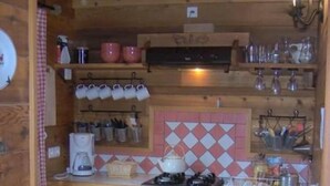 Et lille køkken med træskabe, gasblus, kaffemaskine og flisebeklædt bagvæg.