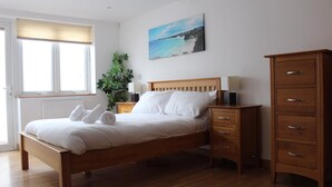 A bedroom with a wooden bed, a nightstand, a dresser, and a large window with blinds.