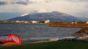 A lakeside view with a mountain in the background, a grassy area, and water sports equipment. - Modern apartment, Residence with swimming pool surrounded by greenery with FREE Wi-Fi (Sirmione)