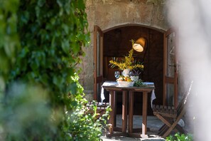 A rustic outdoor dining area with a wooden table set for two, a wicker basket with fruits, and a potted plant. - Villa Els Olivers / Olivers Petits (Alcúdia)
