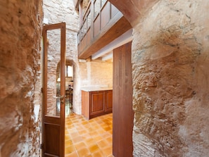A rustic interior with a stone wall, wooden door, and a kitchen area with a tiled floor.