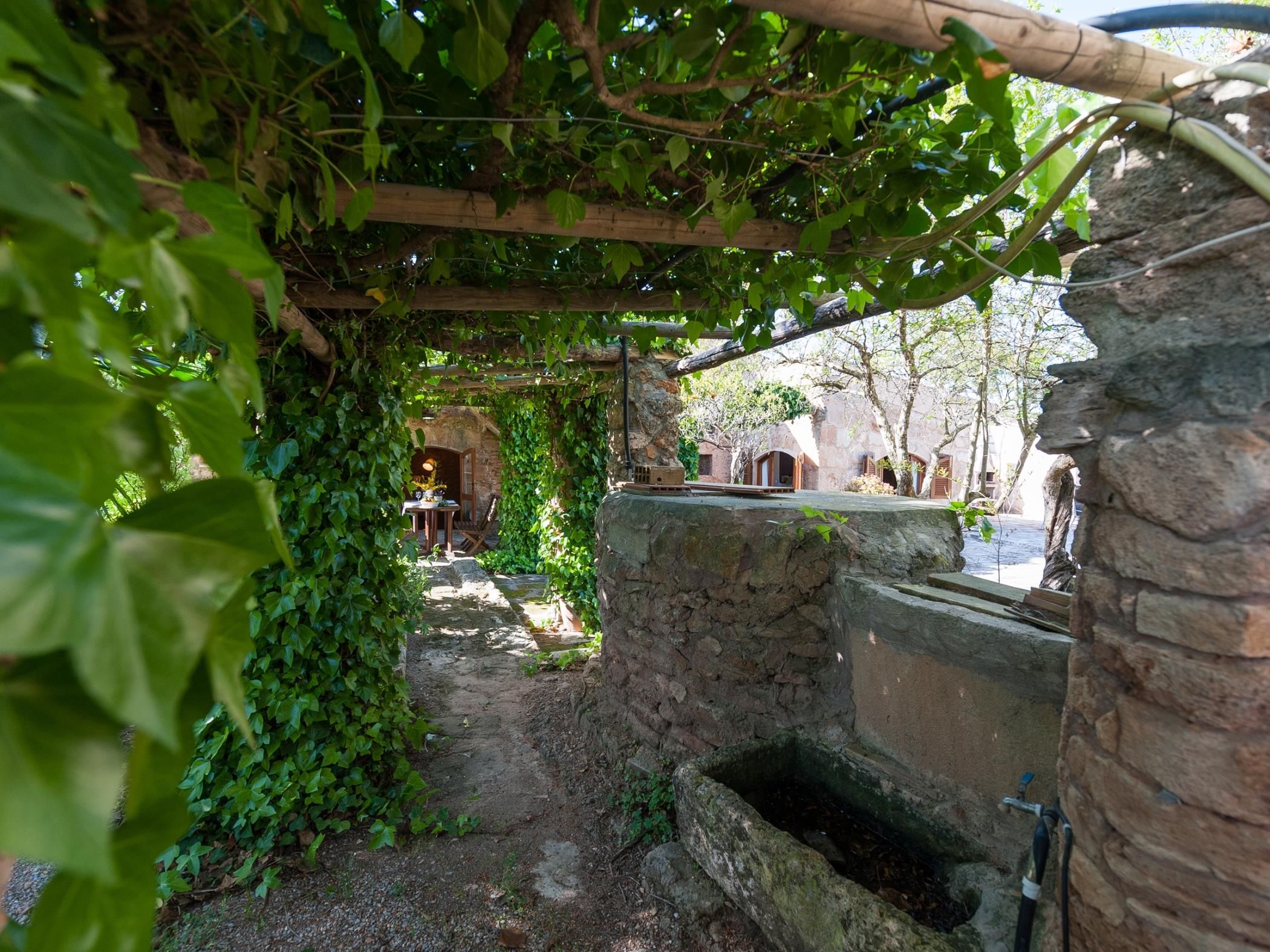 A rustic outdoor area with a stone well, wooden beams, and greenery.