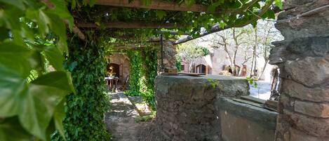 A rustic outdoor area with a stone well, wooden beams, and greenery.