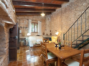 A rustic interior with a wooden table, chairs, a sofa, and a staircase.