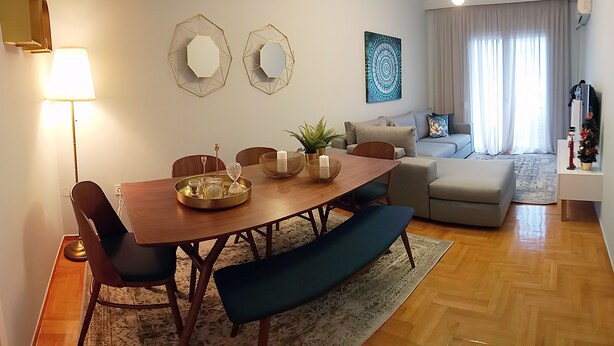 A modern living room with a wooden dining table, blue upholstered chairs, and a grey sofa.