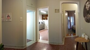 A hallway with a kitchen area visible through an open door, a small table with a chair, and a wall-mounted thermostat.