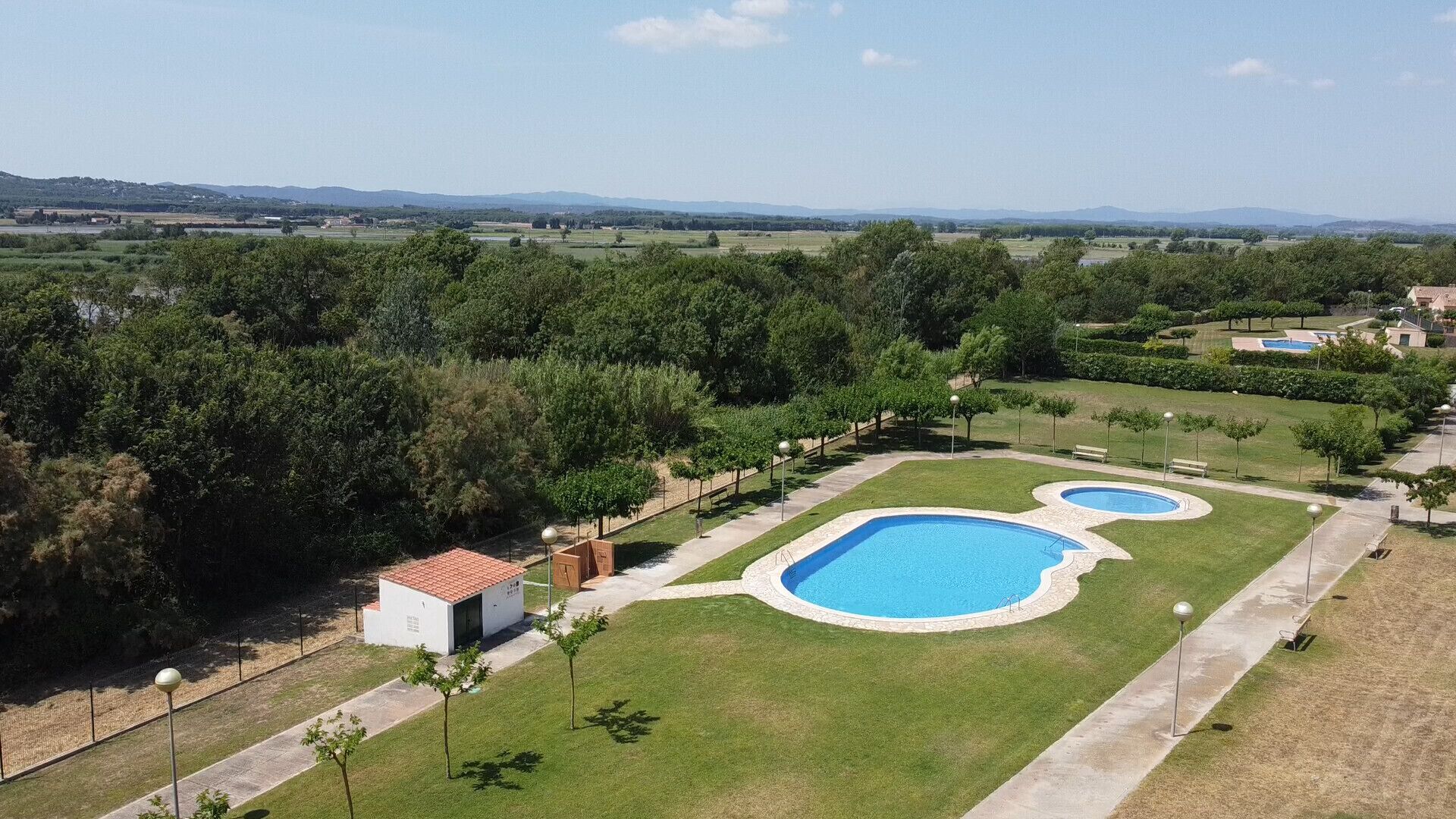 A large outdoor swimming pool area with multiple pools, surrounded by well-maintained lawns and trees.