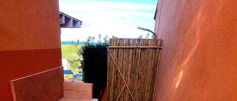 A narrow outdoor patio with a sink, a wooden bench, and a bamboo fence.