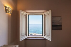 A room with a window overlooking the sea, a wall-mounted light fixture, and a framed picture. - Apartment with terrace and view of the sea (Alghero)