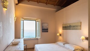 Een slaapkamer met een houten plafond, een bed, een bureau, een raam met uitzicht en een schilderij aan de muur.