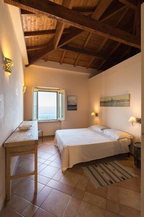 A bedroom with a wooden ceiling, a bed, a desk, a window with a view, and a painting on the wall. - Apartment with terrace and view of the sea (Alghero)