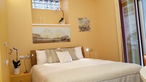 Een slaapkamer met een bed, een nachtkastje, een wandplank met decoratieve objecten en een raam met gordijnen.