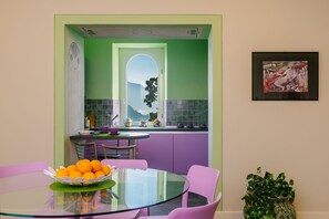 Een moderne keuken met een groene en paarse kleurenschema, een glazen eettafel en een schaal oranjes.