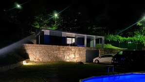 A modern house with a stone wall, a swimming pool, and a car parked outside.