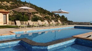 Una piscina con lettini e ombrelloni, circondata da un muro in pietra e da una collina.