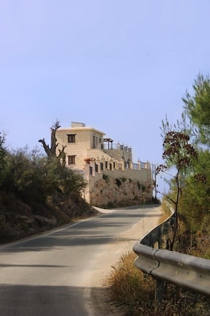 A stone building with a sloped roof, located beside a road with a guardrail.