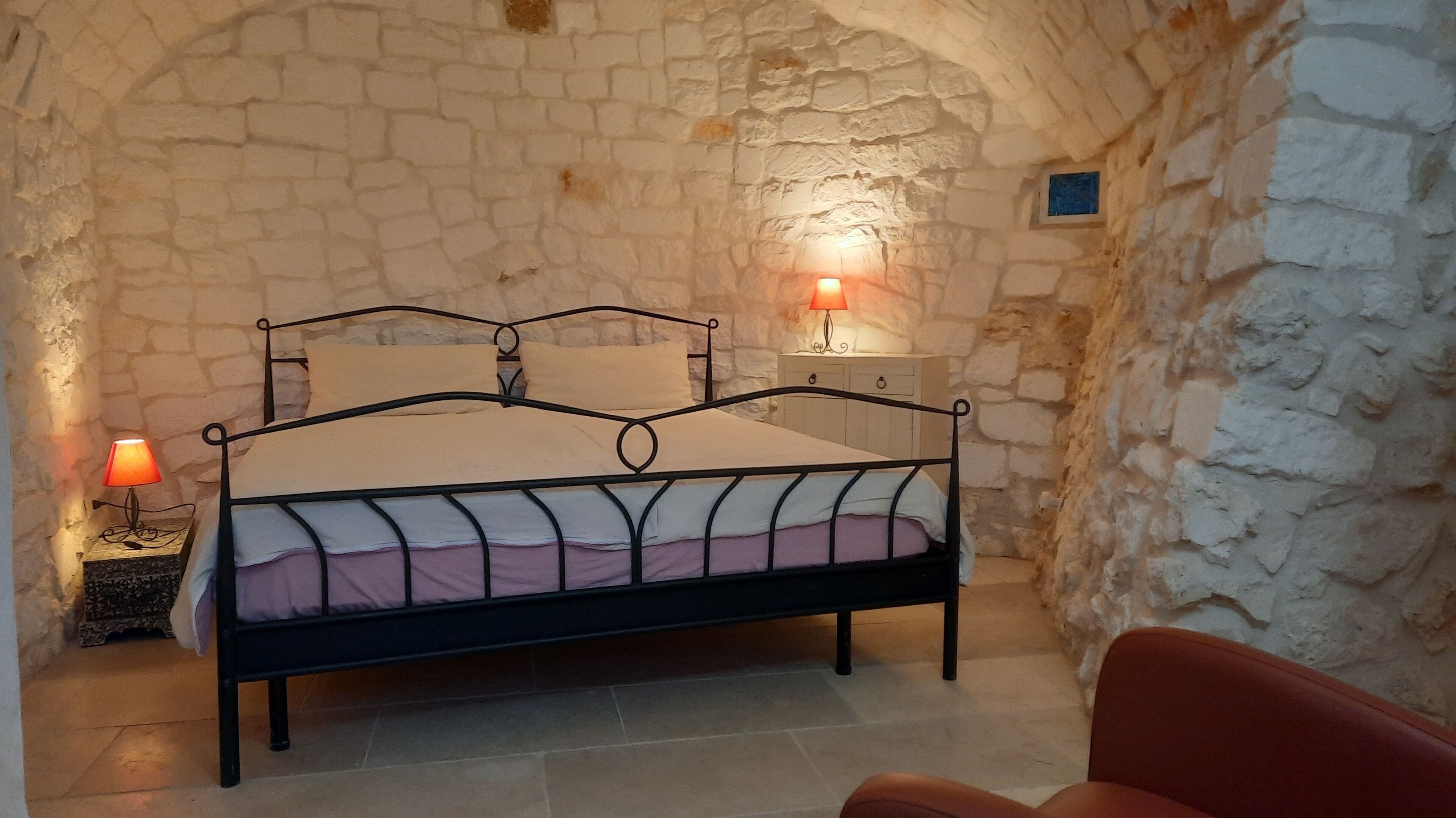 A bed in a stone-walled room with two bedside lamps.