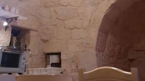 Um interior rústico com teto de pedra, luminária pendente, cadeira de madeira e uma mesa com uma tigela.