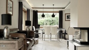 A modern living room with a sofa, a coffee table, a dining table with chairs, and a fireplace. - Popular, Stylish Chalet. Exceptional location with stunning Mont Blanc views. (Chamonix-Mont-Blanc)