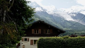 A chalet with a stone foundation, wooden shutters, and a view of snow-capped mountains. - Popular, Stylish Chalet. Exceptional location with stunning Mont Blanc views. (Chamonix-Mont-Blanc)