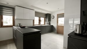 A modern kitchen with dark countertops, a central island, and a view of the outdoors through large windows. - Popular, Stylish Chalet. Exceptional location with stunning Mont Blanc views. (Chamonix-Mont-Blanc)