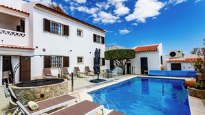 A poolside area with lounge chairs, a stone fire pit, and a clear blue sky.