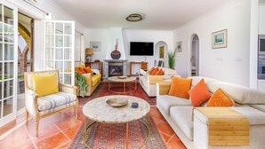 A living room with a fireplace, a television, and a sofa with orange cushions.