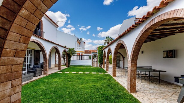 A courtyard with a green lawn, white walls, and brick arches.