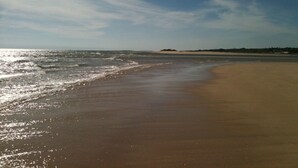 A wide sandy beach with gentle waves and a clear sky.