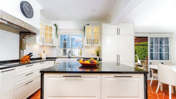 A modern kitchen with white cabinetry, a black countertop, and a bowl of fruit.