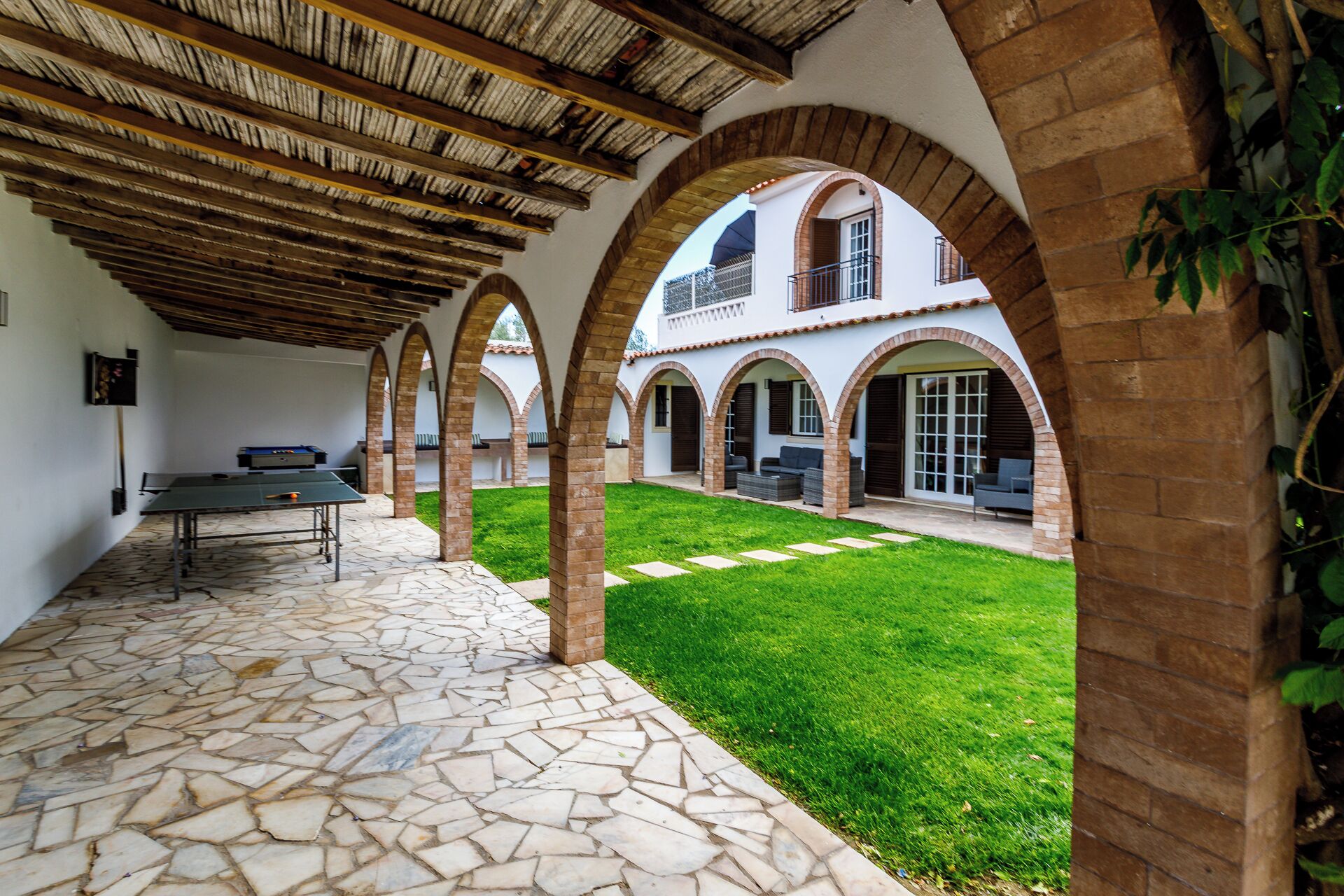 A courtyard with a ping pong table, stone flooring, and arched brick columns.