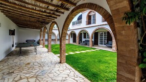 A courtyard with a ping pong table, stone flooring, and arched brick columns.