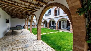 A courtyard with a ping pong table, stone flooring, and arched brick columns.