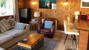 A cozy living room with a sofa, armchair, coffee table, and a dining area with a bar stool. - Detached Cottage In Heart Of This Beautiful Harbour Village (Seahouses)