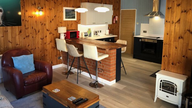 A cozy living room with a leather chair, a coffee table, and a TV. There's a kitchen area with a stove, microwave, and a small dining table. - Detached Cottage In Heart Of This Beautiful Harbour Village (Seahouses)