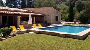 Une piscine avec des chaises longues, un bâtiment en pierre et une pelouse.