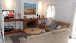 A living room with a sofa, a television, a fireplace, and a painting on the wall. - 3 bedroom villa in Golf Resort, quiet, walking distance to beach, parking, pool (Torrequebrada Golf)