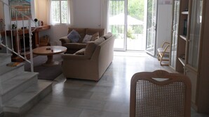 A spacious living room with a beige sofa, a round coffee table, and a staircase leading to an upper floor. - 3 bedroom villa in Golf Resort, quiet, walking distance to beach, parking, pool (Torrequebrada Golf)