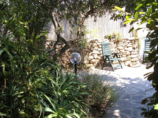 A stone wall, a wooden fence, and a stone pathway leading to a seating area with two chairs.