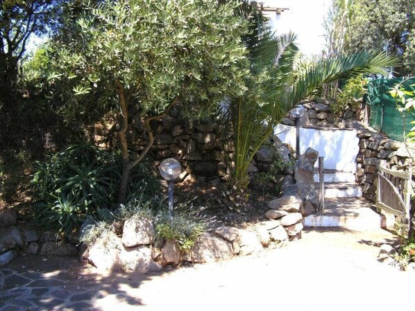 A garden with a stone wall, a metal gate, and various plants. - Typical house in the countryside, only a few km from the sandy beach (Aglientu)