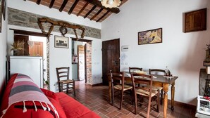 Een gezellige woonkamer met een rode bank, een eethoek met houten stoelen en een tafel, en een keuken die door een open deur zichtbaar is.