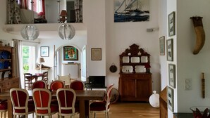 Un comedor con una mesa de madera y sillas rojas, un espejo sobre la mesa y un cuadro de un velero en la pared.