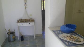 A room with a small white table with drawers, a blue decorative pillow, a plate of seashells, a metal bucket, and a wooden bucket.
