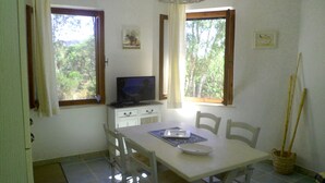 A small dining area with a table, chairs, a television, and windows with curtains. - Casa Niperu in the countryside a few meters from the beaches of Cala Ginepro (Cala Liberotto)