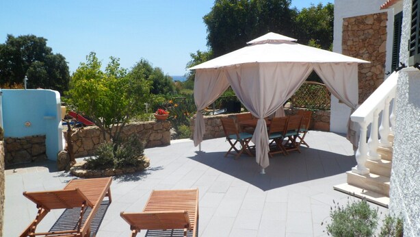 An outdoor patio with a covered dining area, stone walls, and a view of the sea. - Casa Niperu in the countryside a few meters from the beaches of Cala Ginepro (Cala Liberotto)
