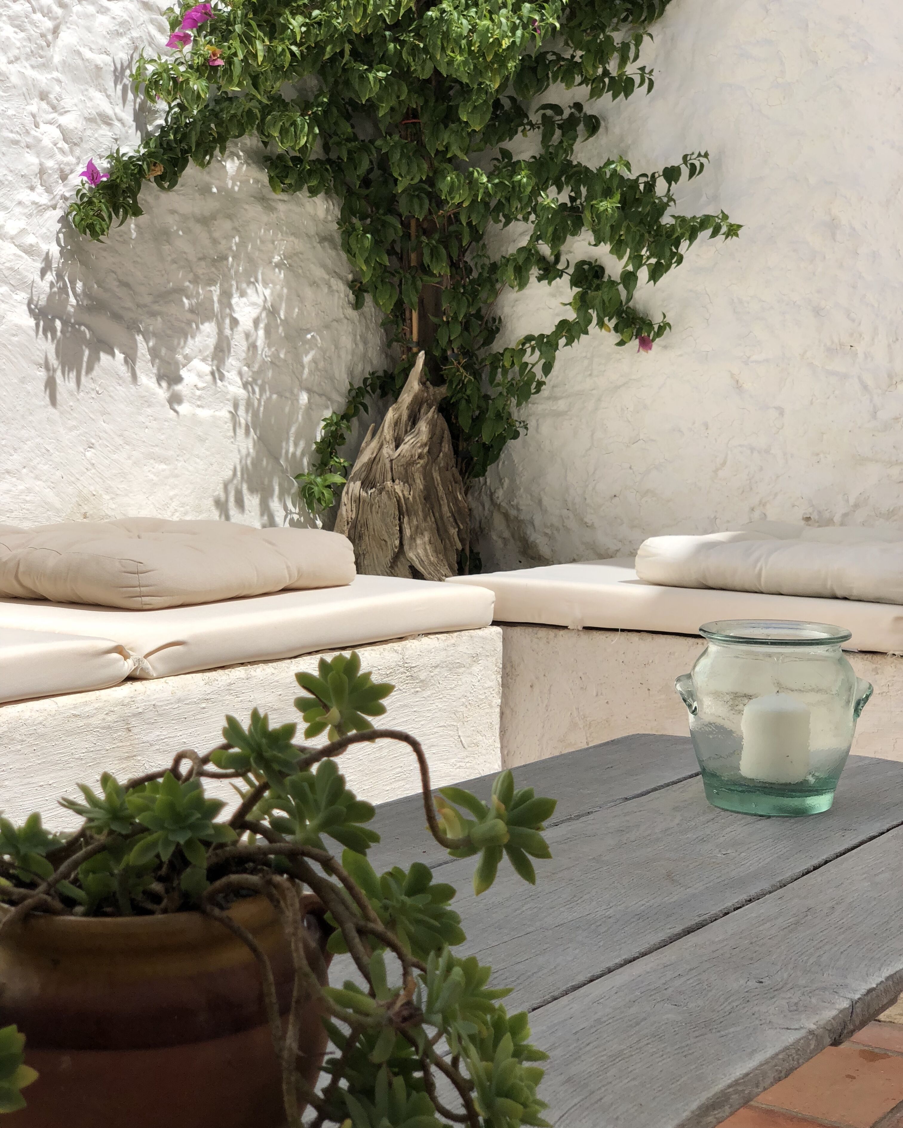A cozy seating area with a cushioned bench, a small table with a glass jar, and a potted plant.