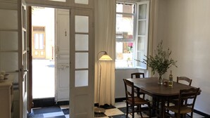 Un comedor con suelo a cuadros, una mesa redonda de madera y sillas. Hay un jarrón con flores sobre la mesa, y una lámpara junto a él.