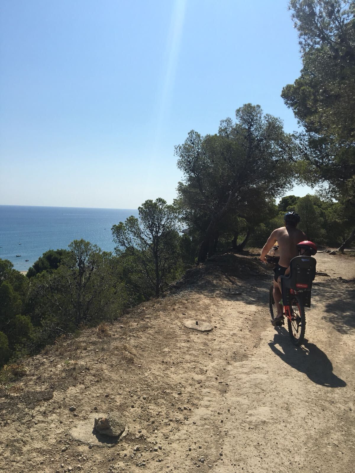 A person riding a bicycle on a dirt path with a view of the sea and trees.