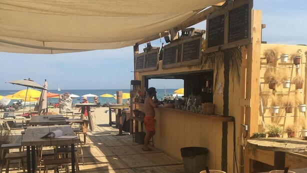 Un área de estar al aire libre con mesas y sillas, una barra y vista a la playa.