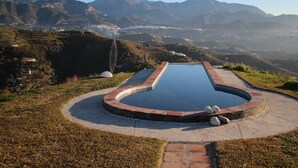 A swimming pool with a curved edge, surrounded by a brick border, set against a mountainous backdrop. - La Bolina-unique romantic holiday experience, private infinity pool, huge views (torrox)